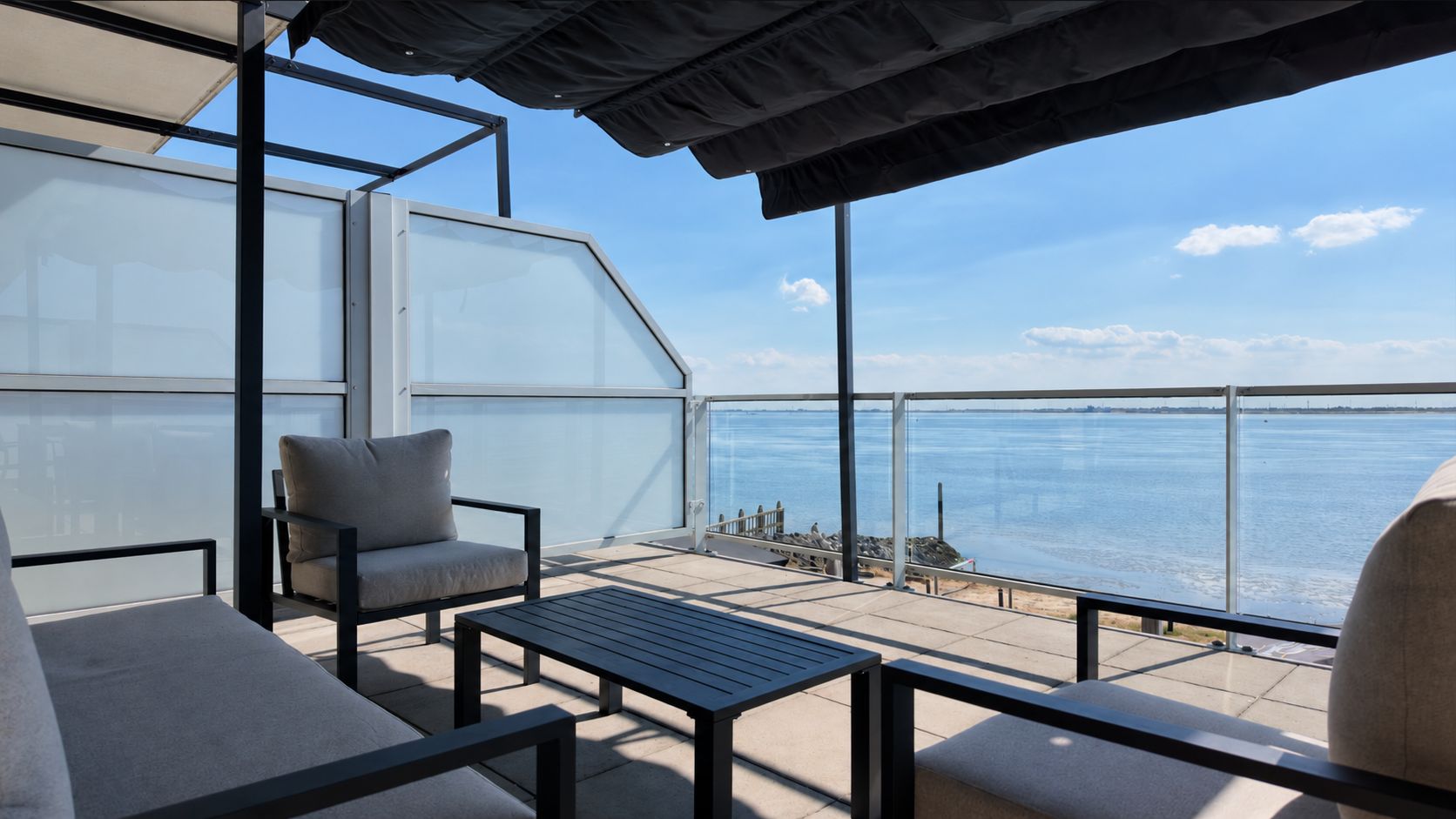 Un balcone con vista sull'acqua, arredato con un divano, una sedia e un tavolo.