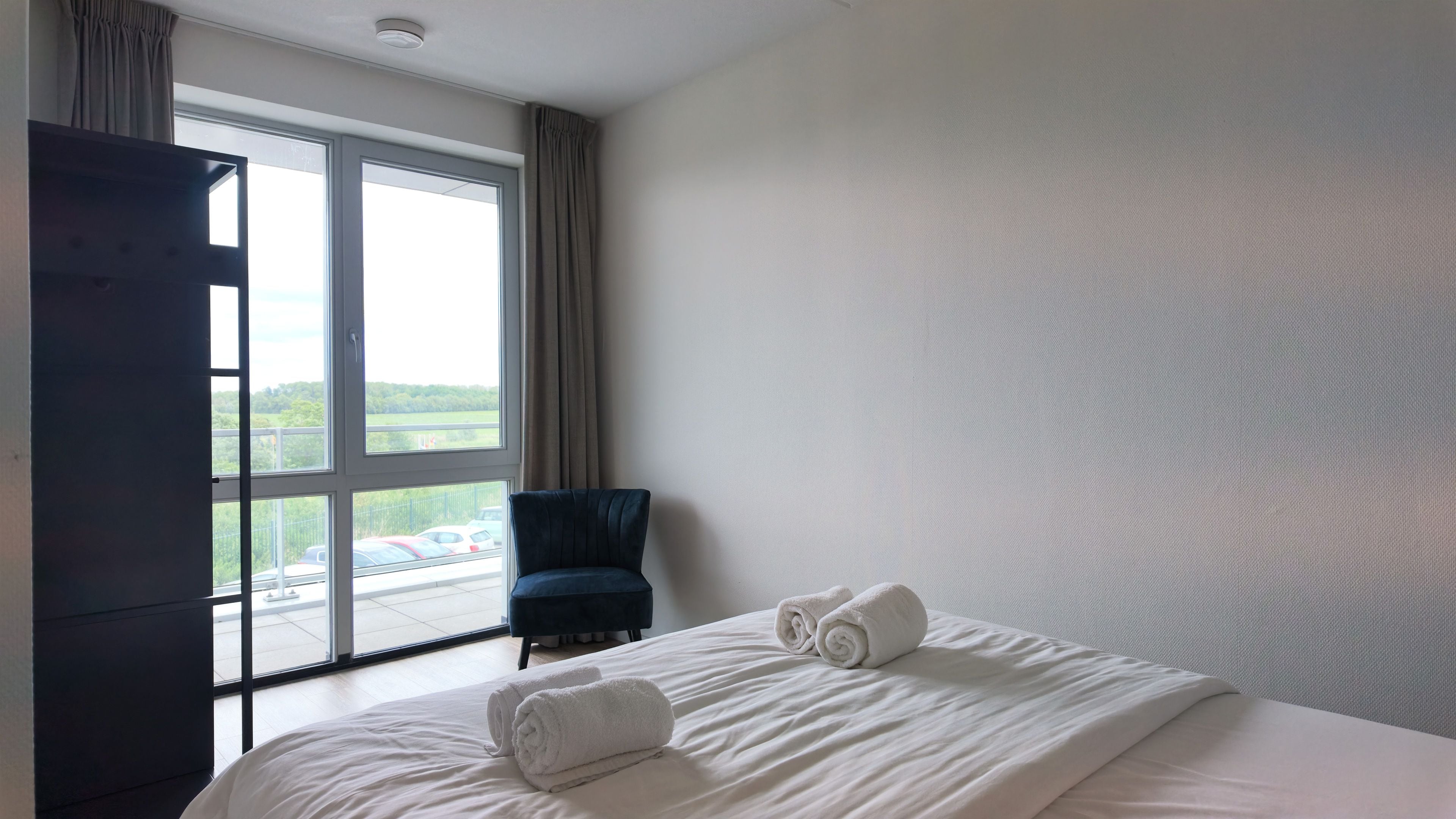 A hotel room with a large window, a bed with white linens, and a dark-colored chair.