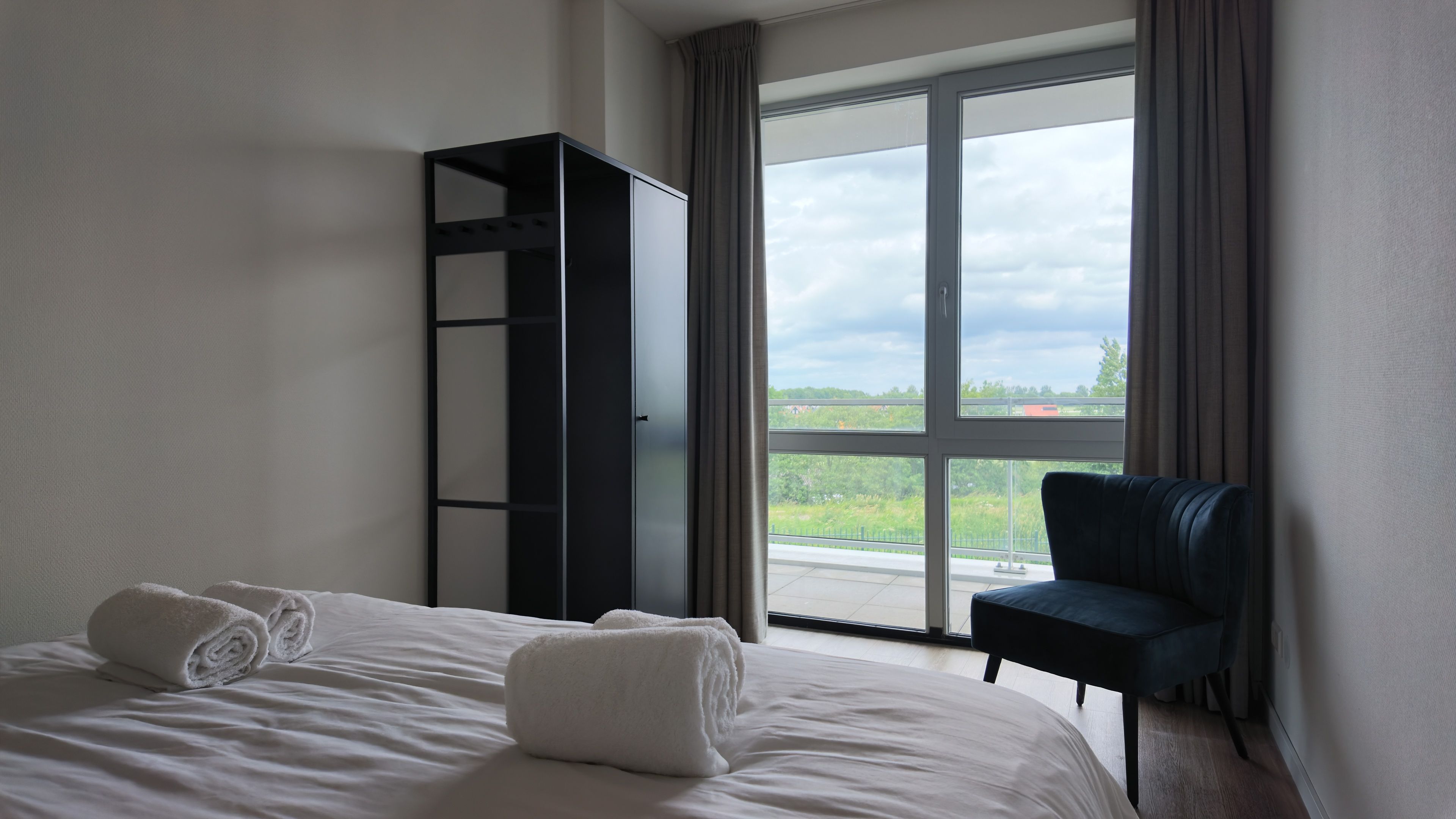 Ein Hotelzimmer mit Bett, Stuhl, Kleiderschrank und einem großen Fenster mit Blick.