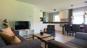 Una sala de estar moderna con un televisor de pantalla plana, sofás, una mesa de centro y un comedor con sillas y una mesa.