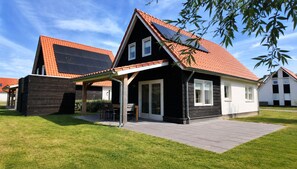 Una casa de dos pisos con techo inclinado, un porche cubierto y paneles solares.