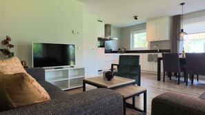 Una sala moderna con un televisor de pantalla plana, un sofá, una mesa de centro y un comedor con sillas y una mesa.