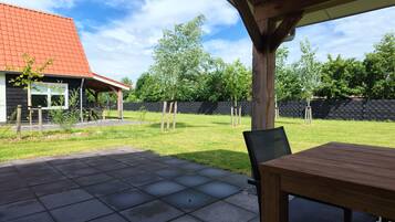 Eine Terrassenfläche mit Tisch und Stühlen, ein überdachter Sitzbereich und der Blick auf ein Haus mit rotem Dach.