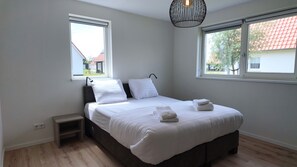 A bedroom with a bed, two windows, a nightstand, and a hanging light fixture.