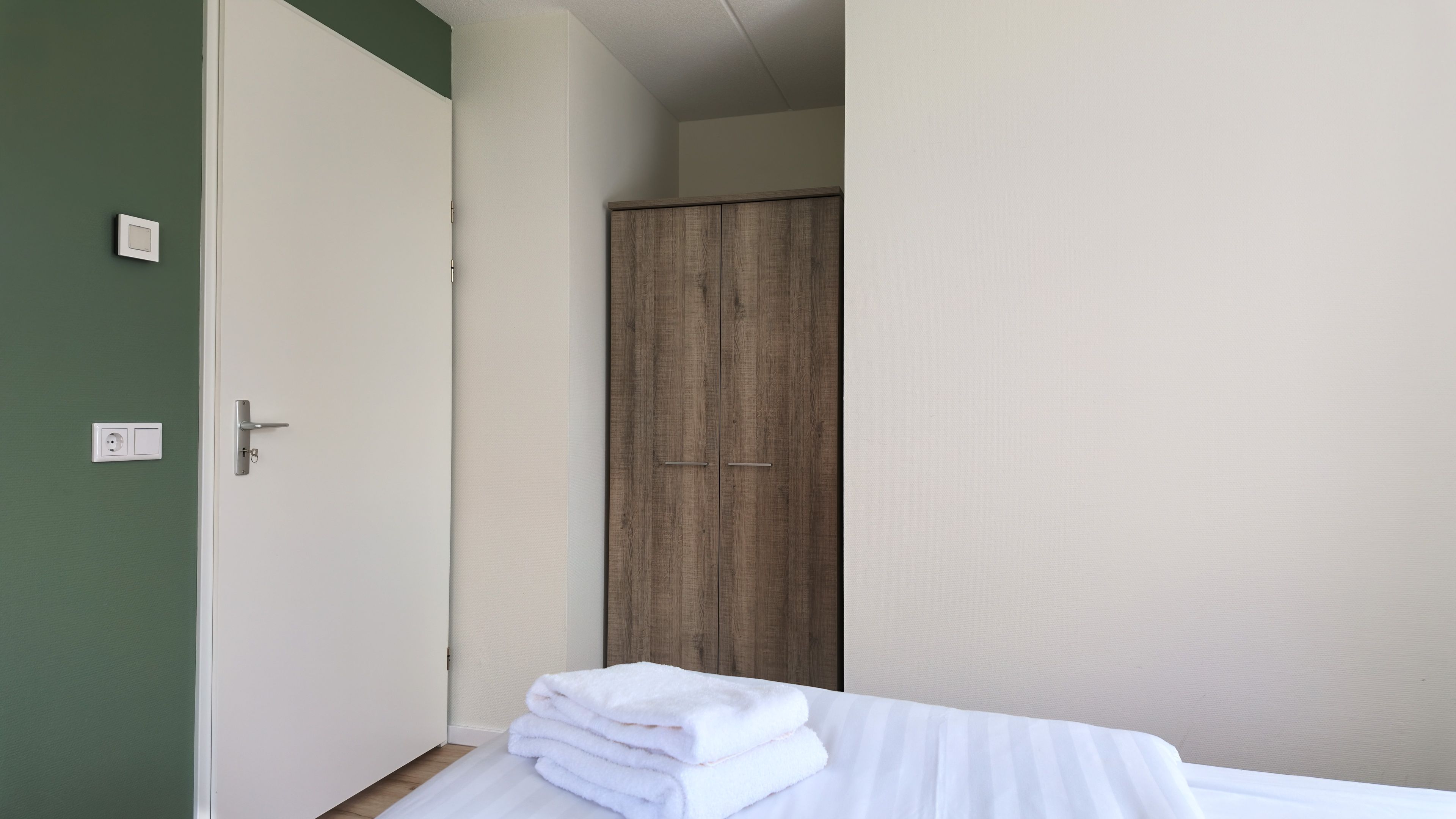 Una stanza con un letto, un armadio e una porta con l'interruttore della luce.
