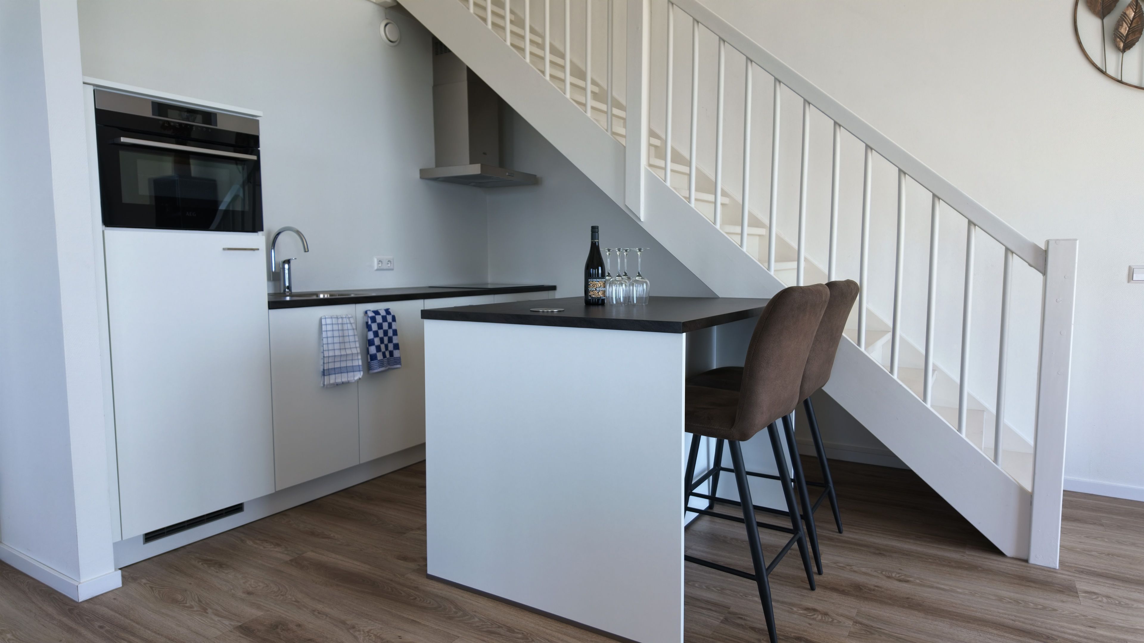 Une cuisine moderne dotée d’un îlot central, d’un four encastré et d’un escalier avec une rampe blanche.