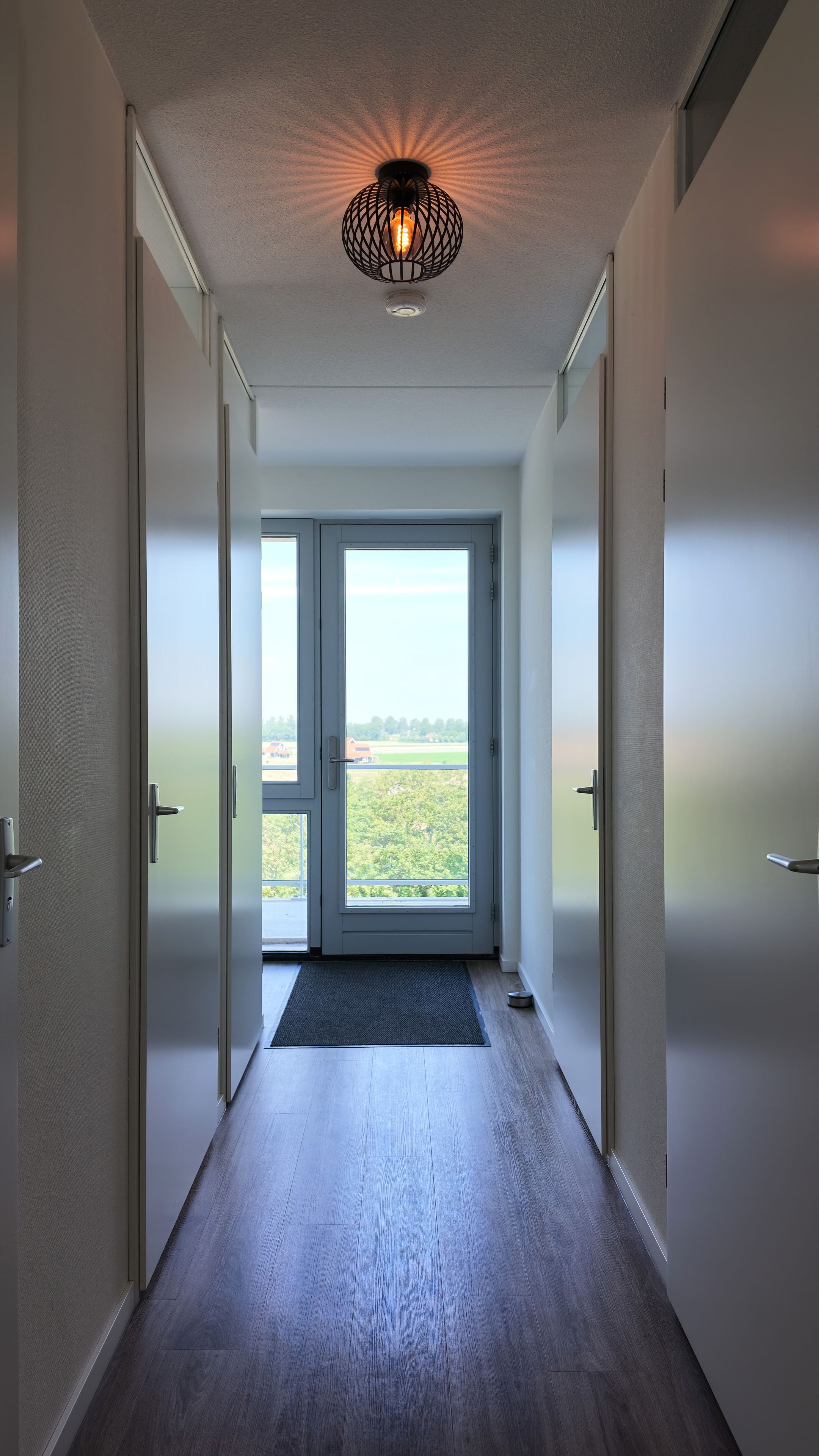 Un corridoio con una porta che dà su un balcone vista su vegetazione e edifici.