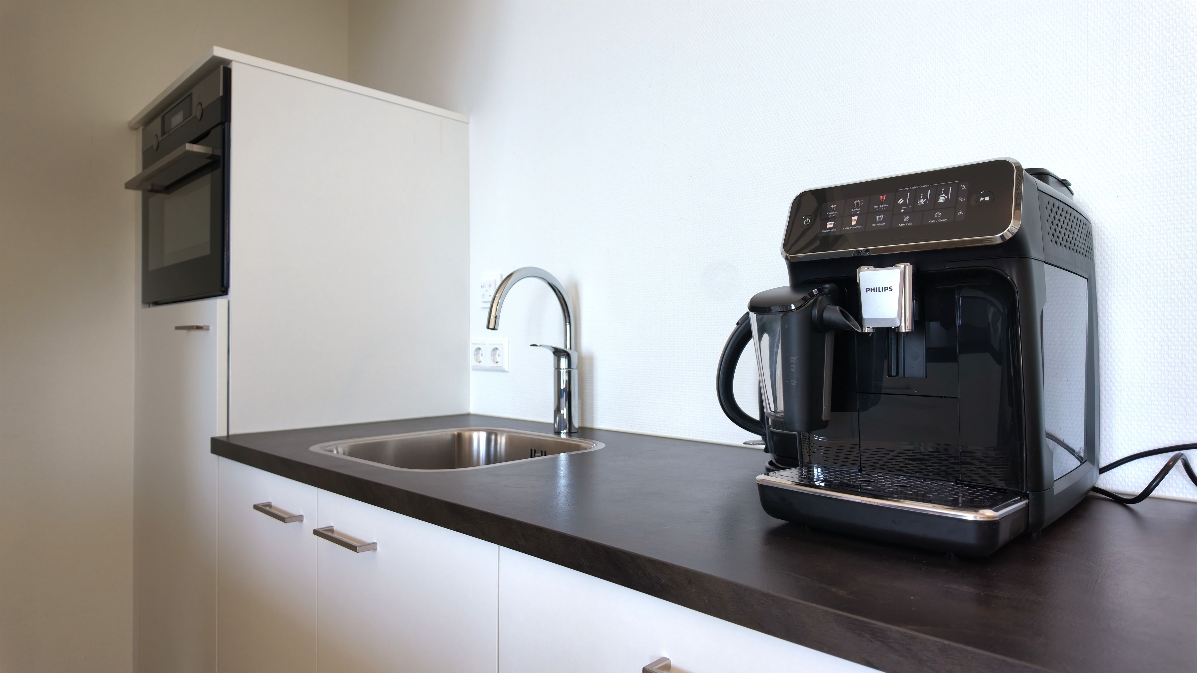 Een moderne keuken met een ingebouwde koffiezetapparaat, een roestvrijstalen spoelbak en een magnetron boven het aanrecht.
