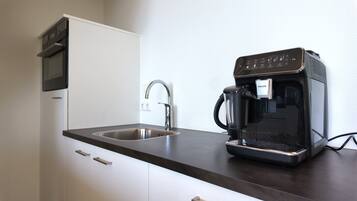 Een moderne keuken met een ingebouwde koffiezetapparaat, een roestvrijstalen spoelbak en een magnetron boven het aanrecht.