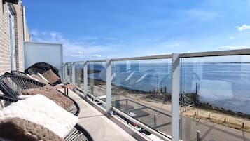 Een balkon met buitenmeubilair, uitzicht op zee en een gebouw met een bakstenen gevel.