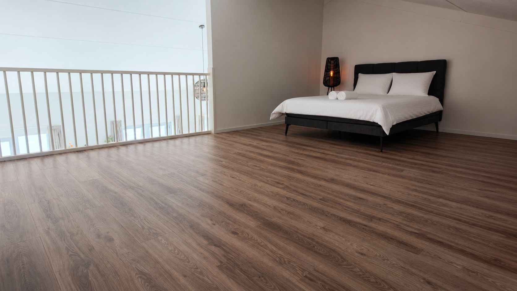 A bedroom with a large window, a bed with white bedding, and a wooden floor.