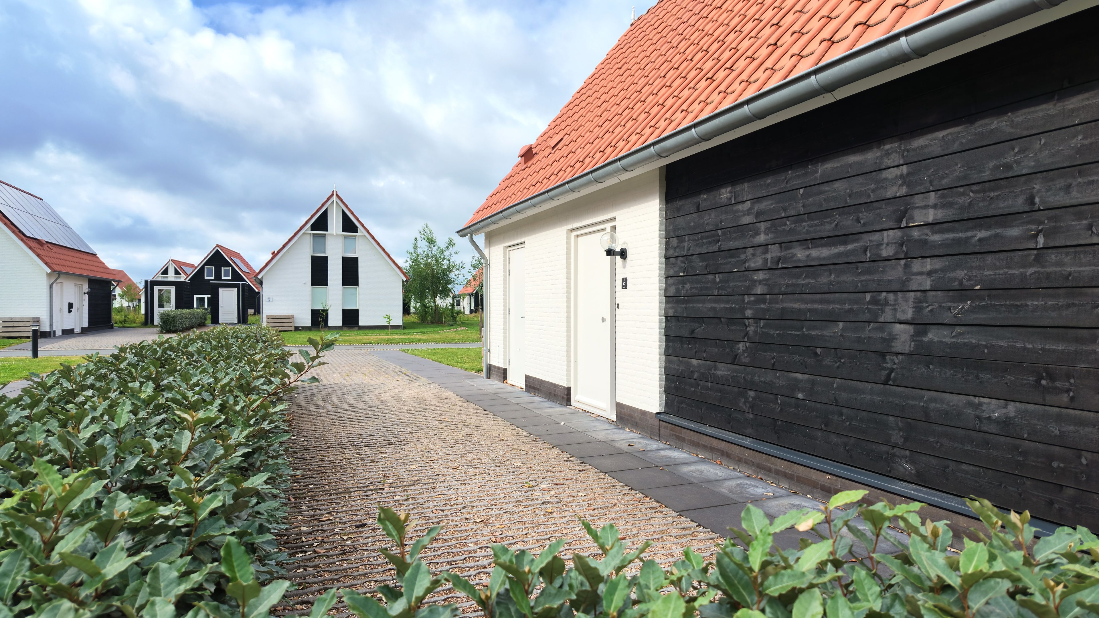 Een woonwijk met een verhard voetpad, een rij huizen met rode dakpannen en een zwart gebouw met een garagepoort.