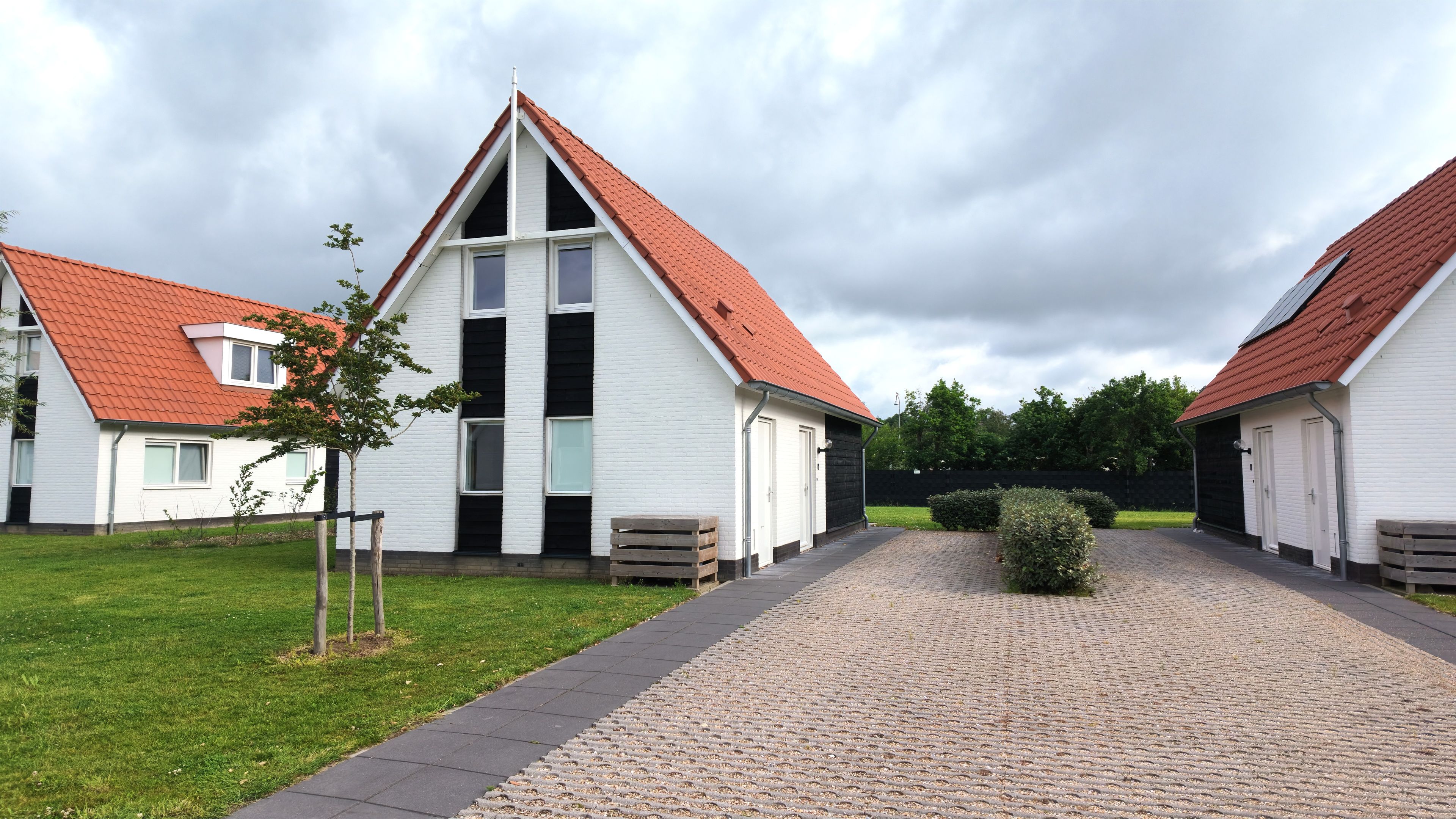 Une rangée de bâtiments blancs aux toits rouges, un chemin piétonnier pavé et un petit arbre.