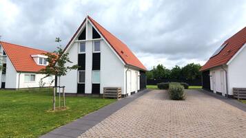 Une rangée de bâtiments blancs aux toits rouges, un chemin piétonnier pavé et un petit arbre.