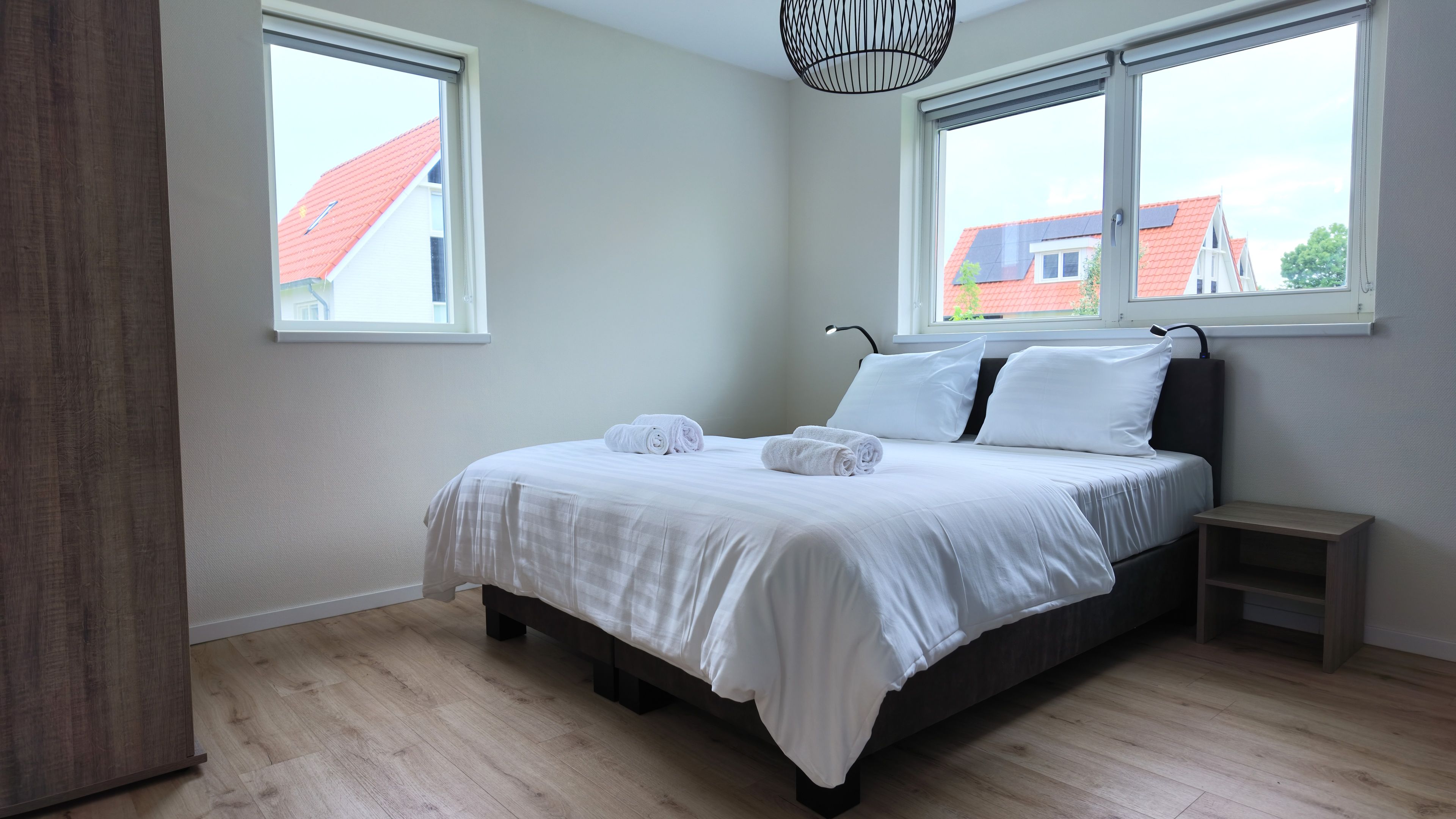 Una camera da letto con un letto, due finestre, un comodino e una lampada a sospensione.
