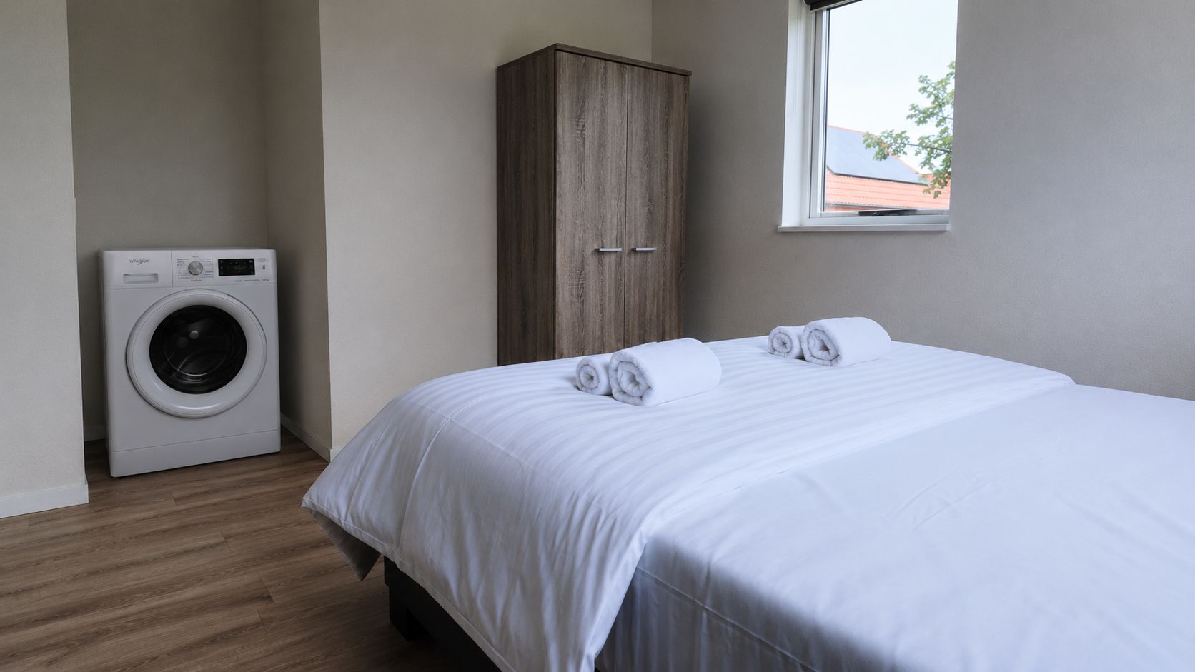 Una camera d'albergo con un letto, un armadio in legno, una lavatrice e una finestra vista edificio.