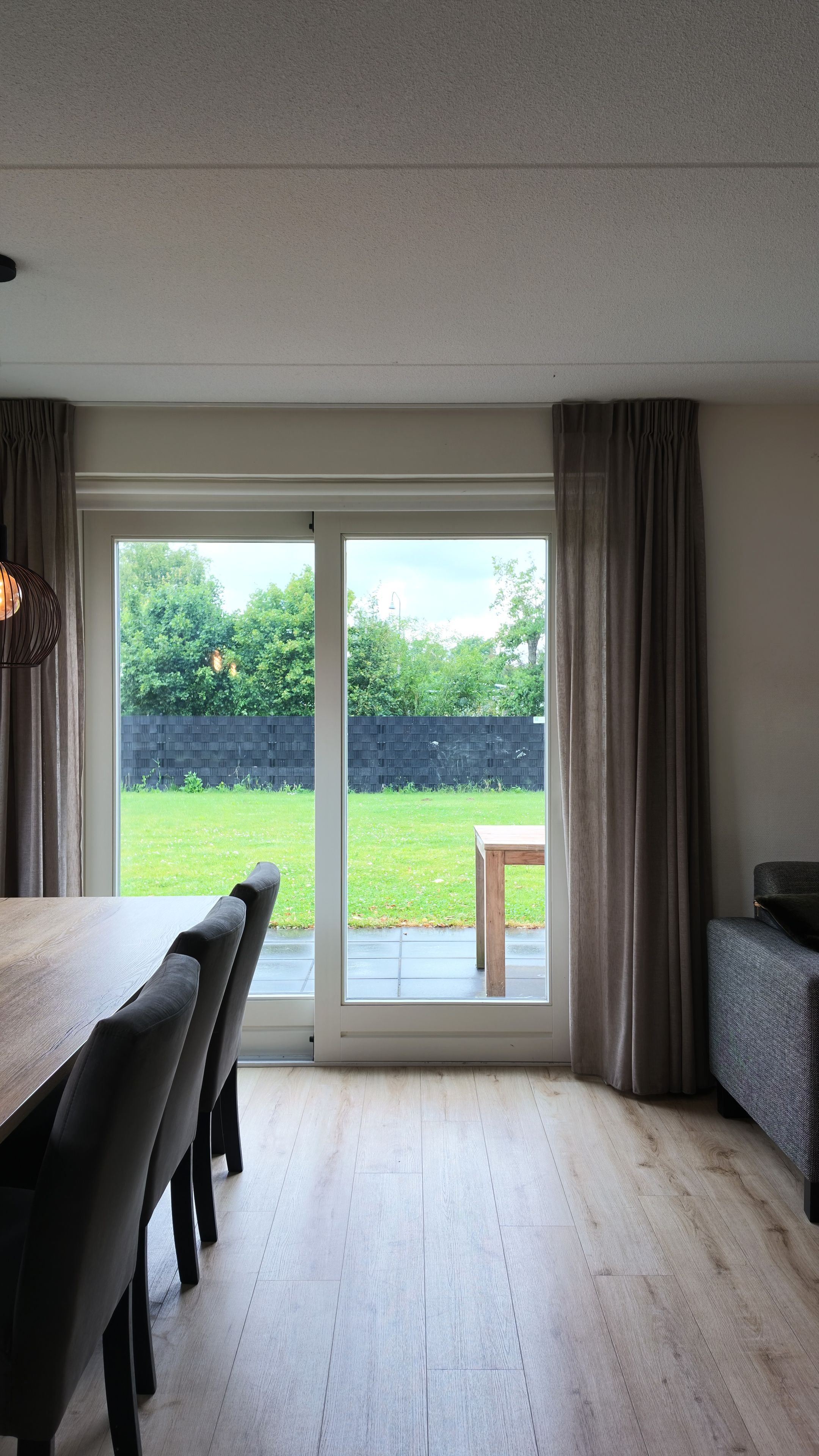 A room with a dining table and chairs, a sofa, and a sliding glass door leading to a garden.