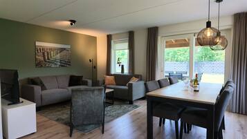 Ein modernes Wohnzimmer mit einer Couch, einem Esstisch mit Stühlen, einem Fernseher und einem Bild an der Wand.