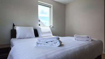 A neatly made bed with white linens and towels, a bedside lamp, and a window with a view of the sky.