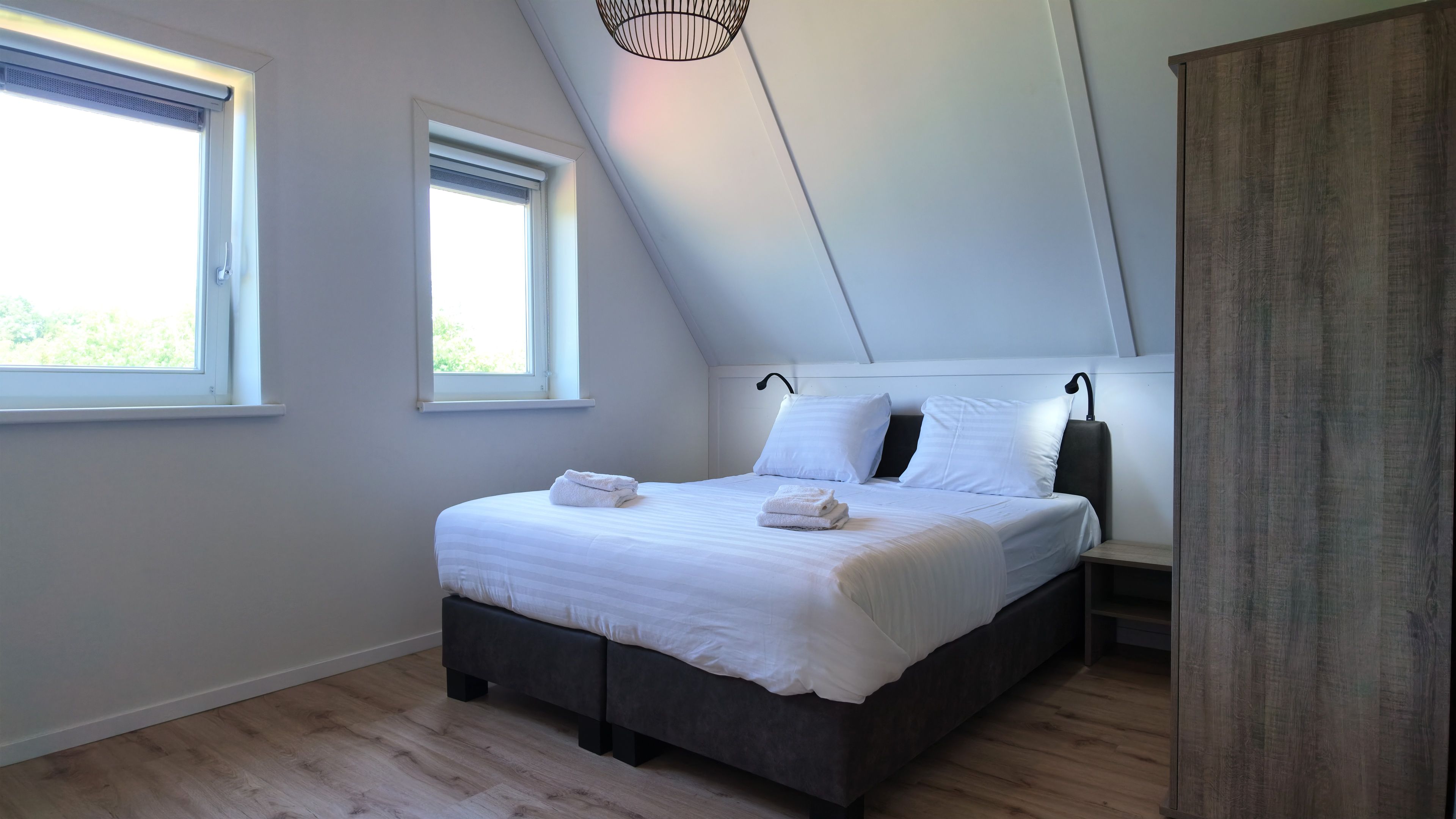 Une chambre à coucher comprenant un lit, deux tables de chevet, une fenêtre et un luminaire au plafond.