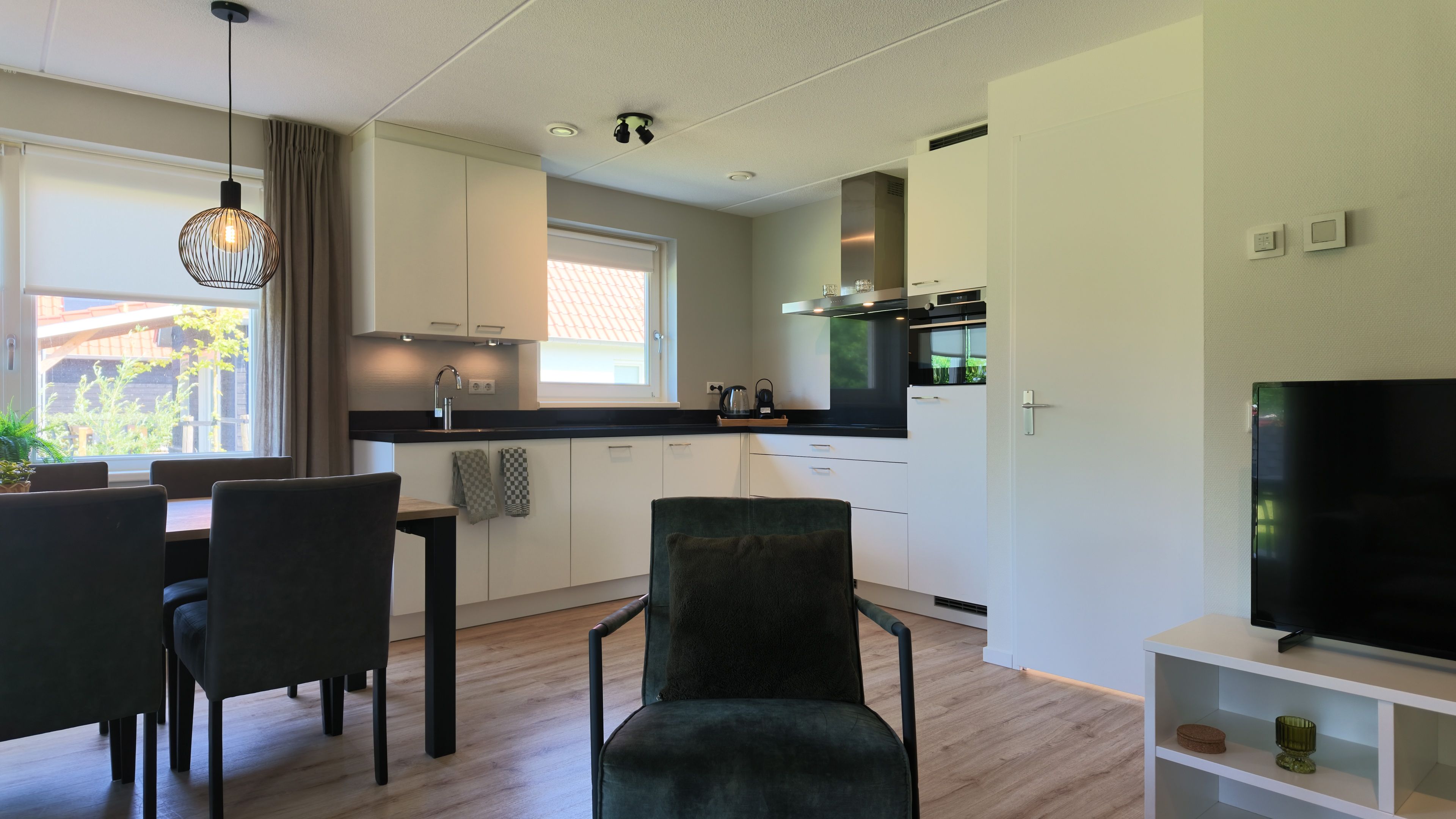 Uma cozinha moderna com armários brancos, uma área de jantar com mesa e cadeiras, e uma TV de tela plana em um suporte.