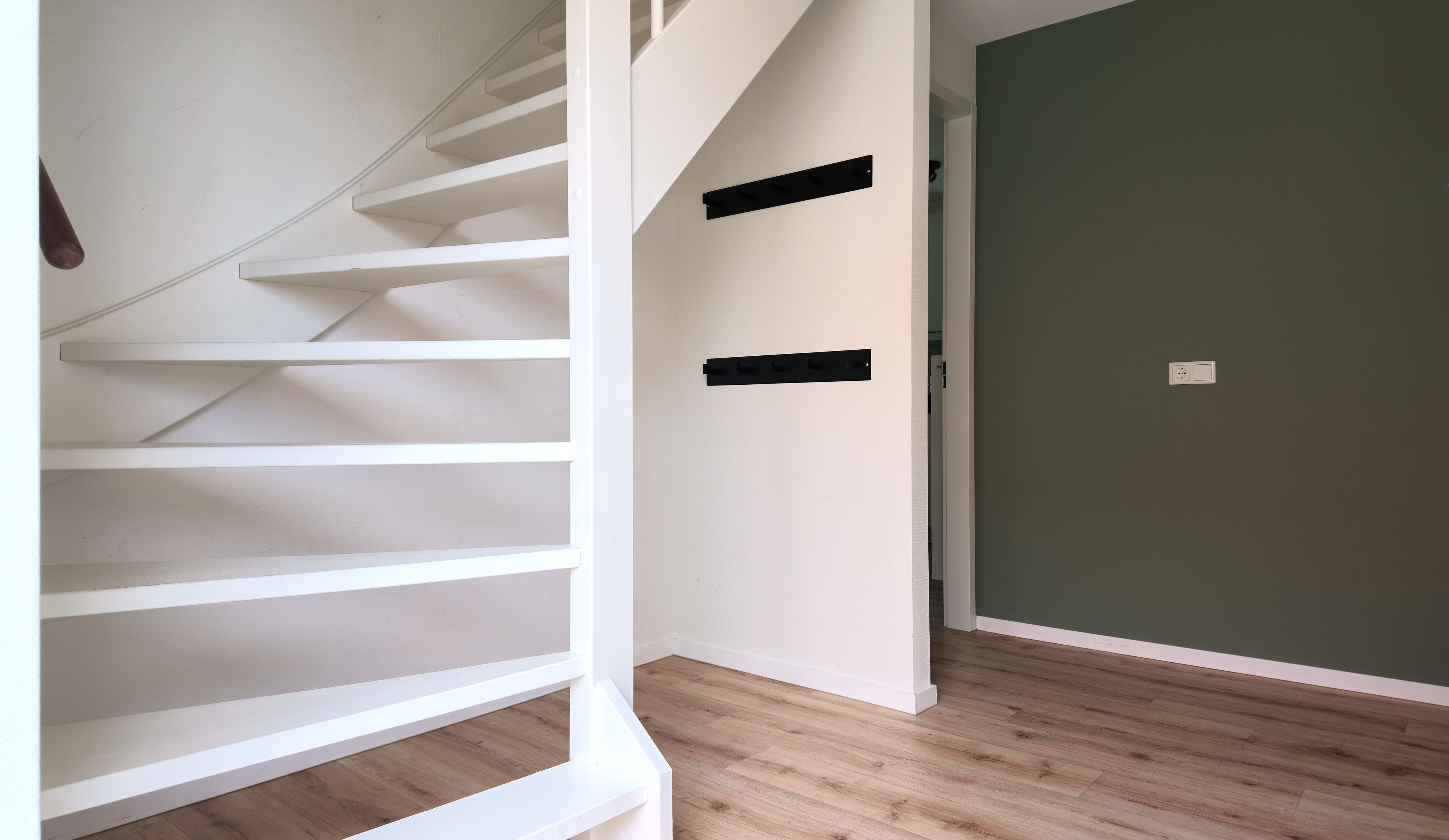 Un escalier avec des rampes blanches et un plancher en bois, menant à une pièce dont un mur est peint en vert et qui possède une porte.