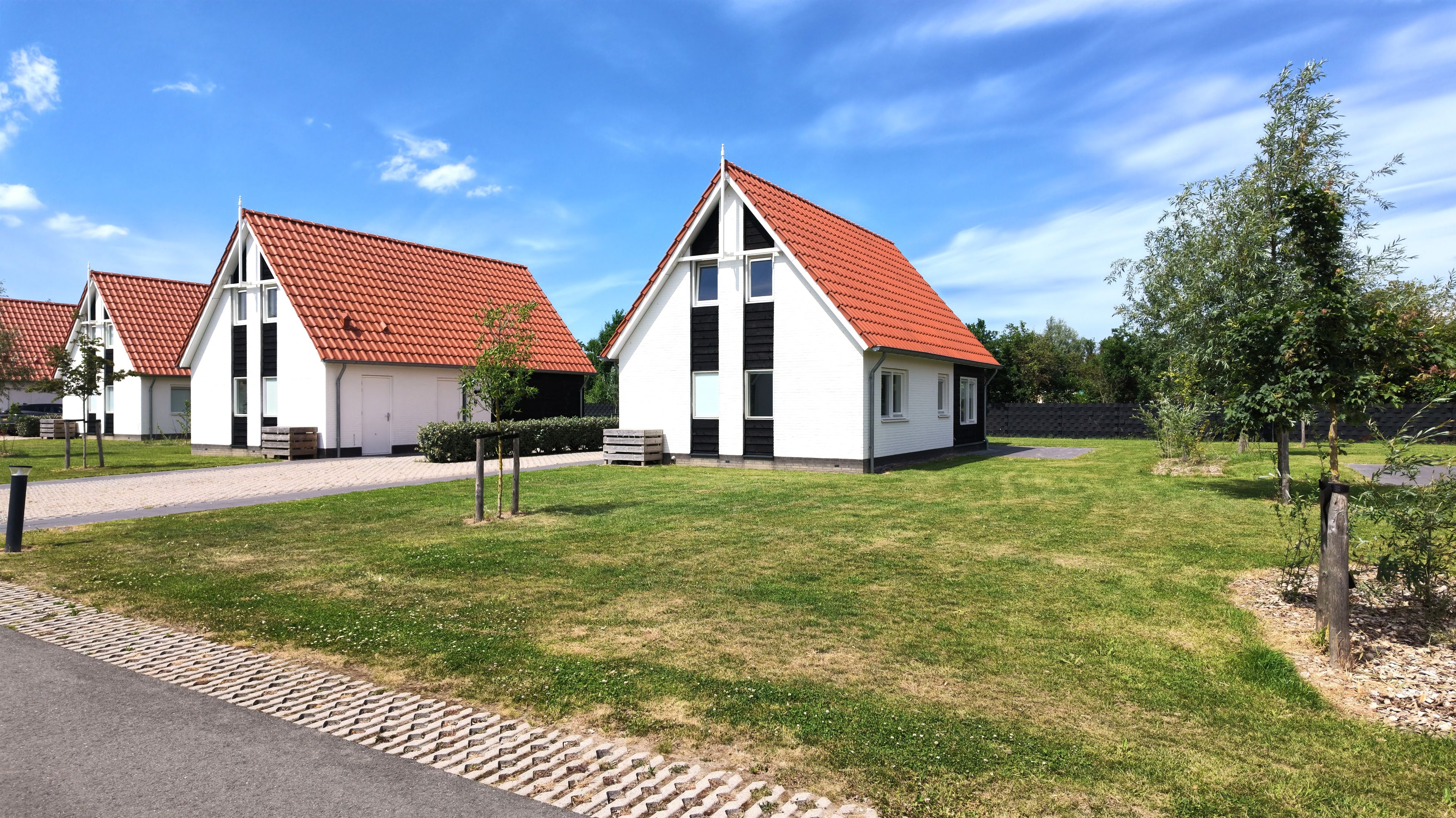 Une rangée de maisons blanches aux toits rouges, un chemin pavé et une zone herbeuse avec des arbres.