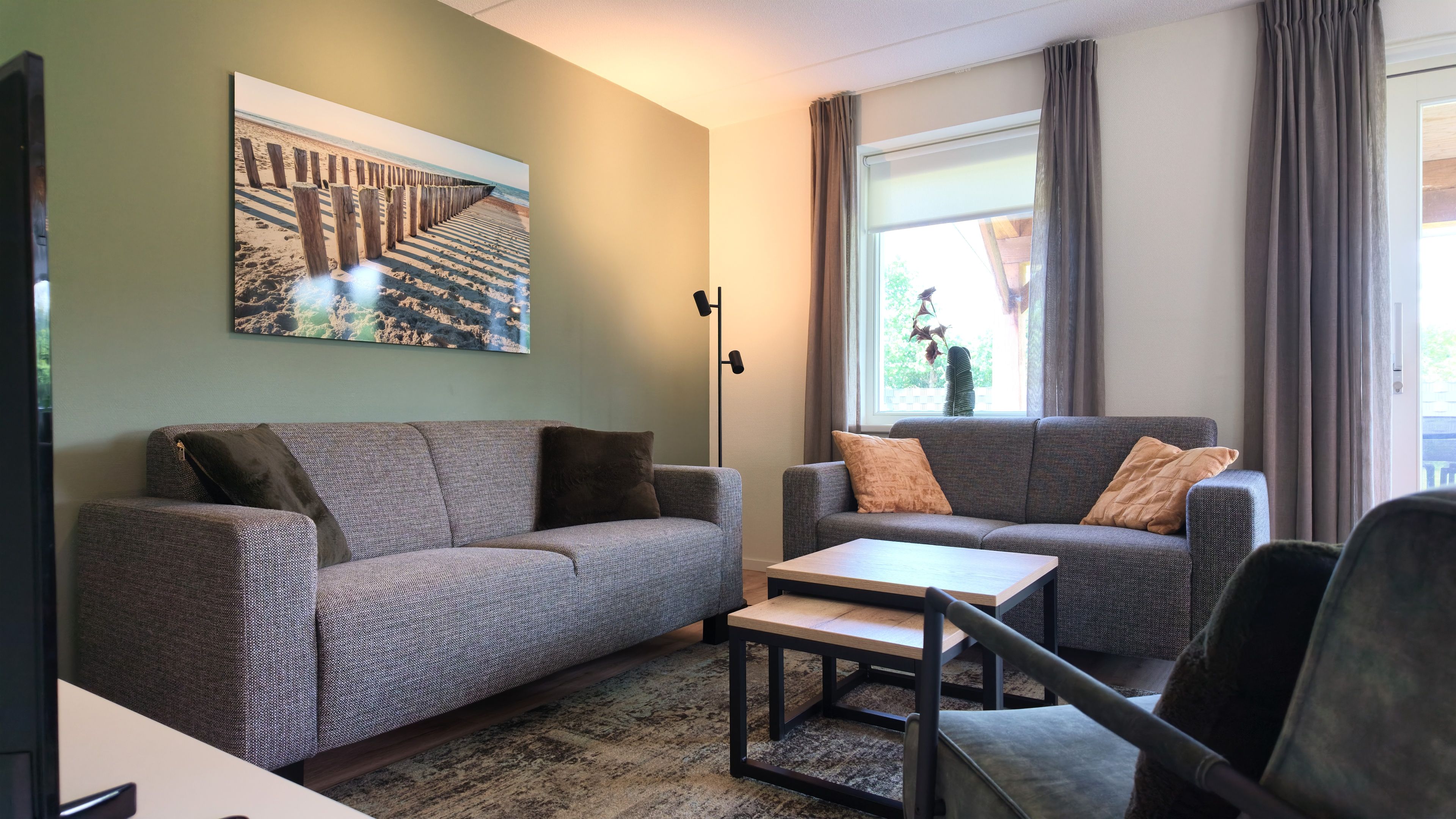 Een woonkamer met twee grijze banken, een salontafel en een vloerlamp.