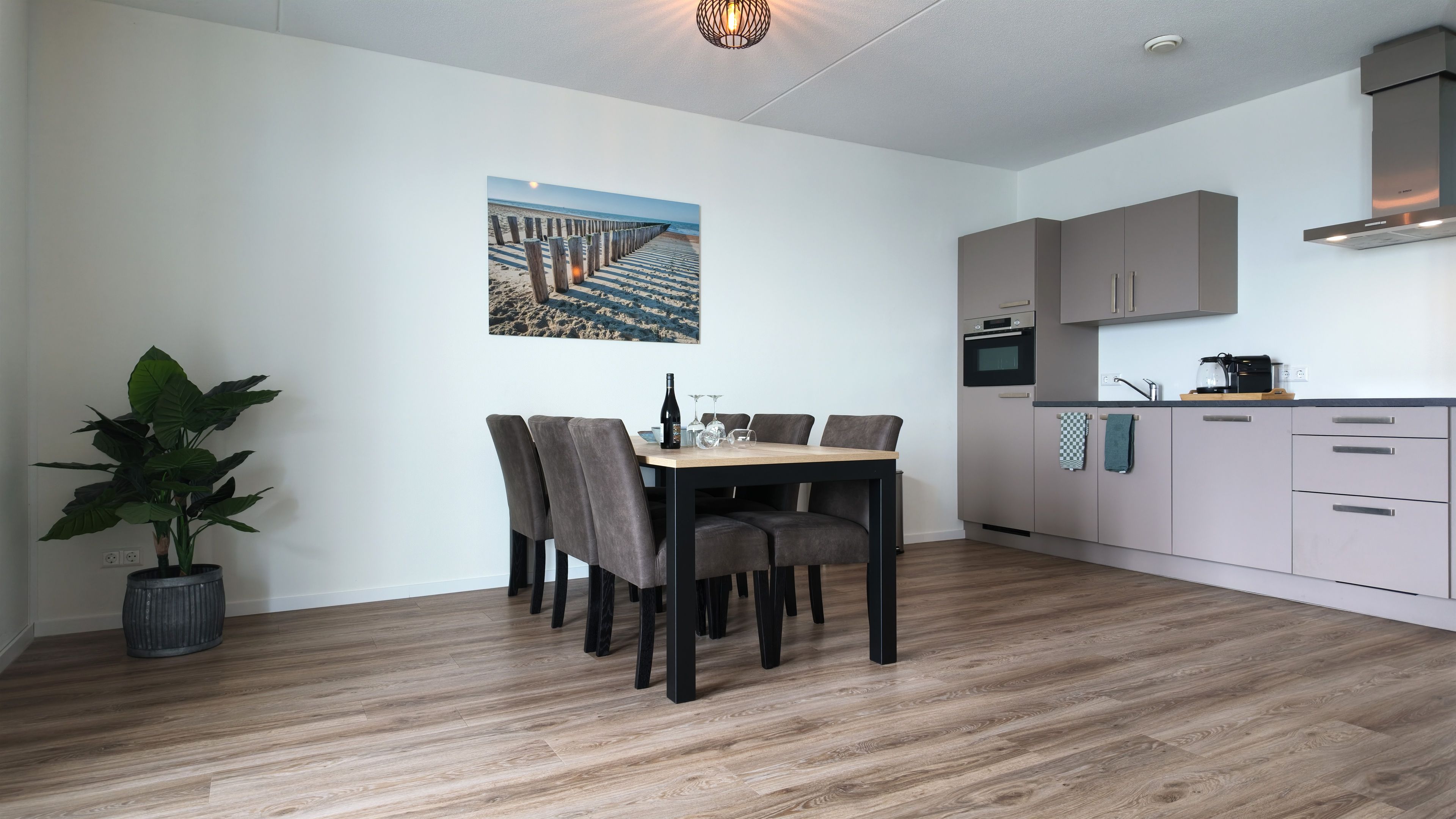 Een moderne keuken met grijze kastjes, een ingebouwde oven en een koffiezetapparaat op het aanrecht.