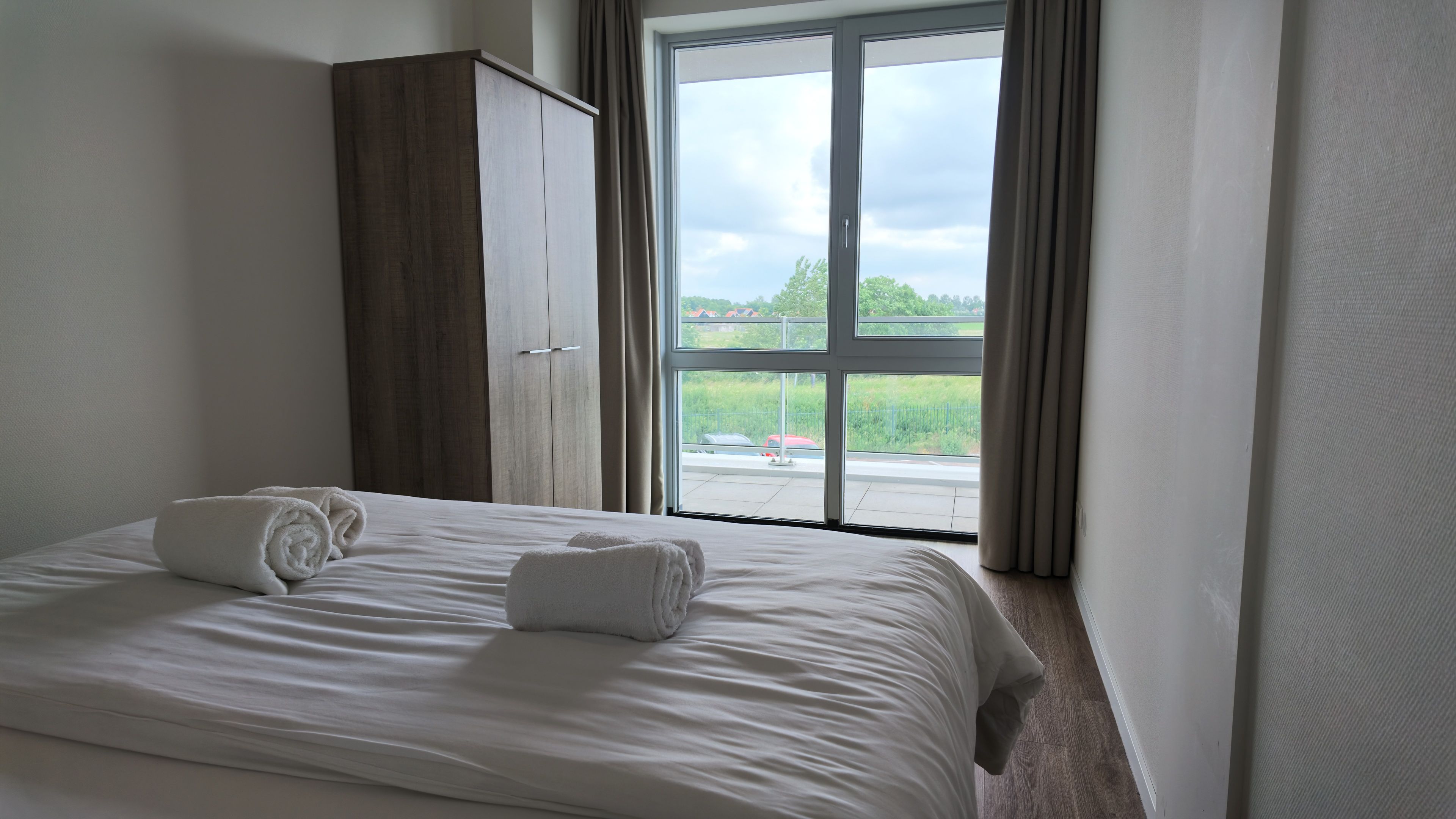 Ein Hotelzimmer mit einem Bett, einem Kleiderschrank und einem großen Fenster mit Vorhängen.