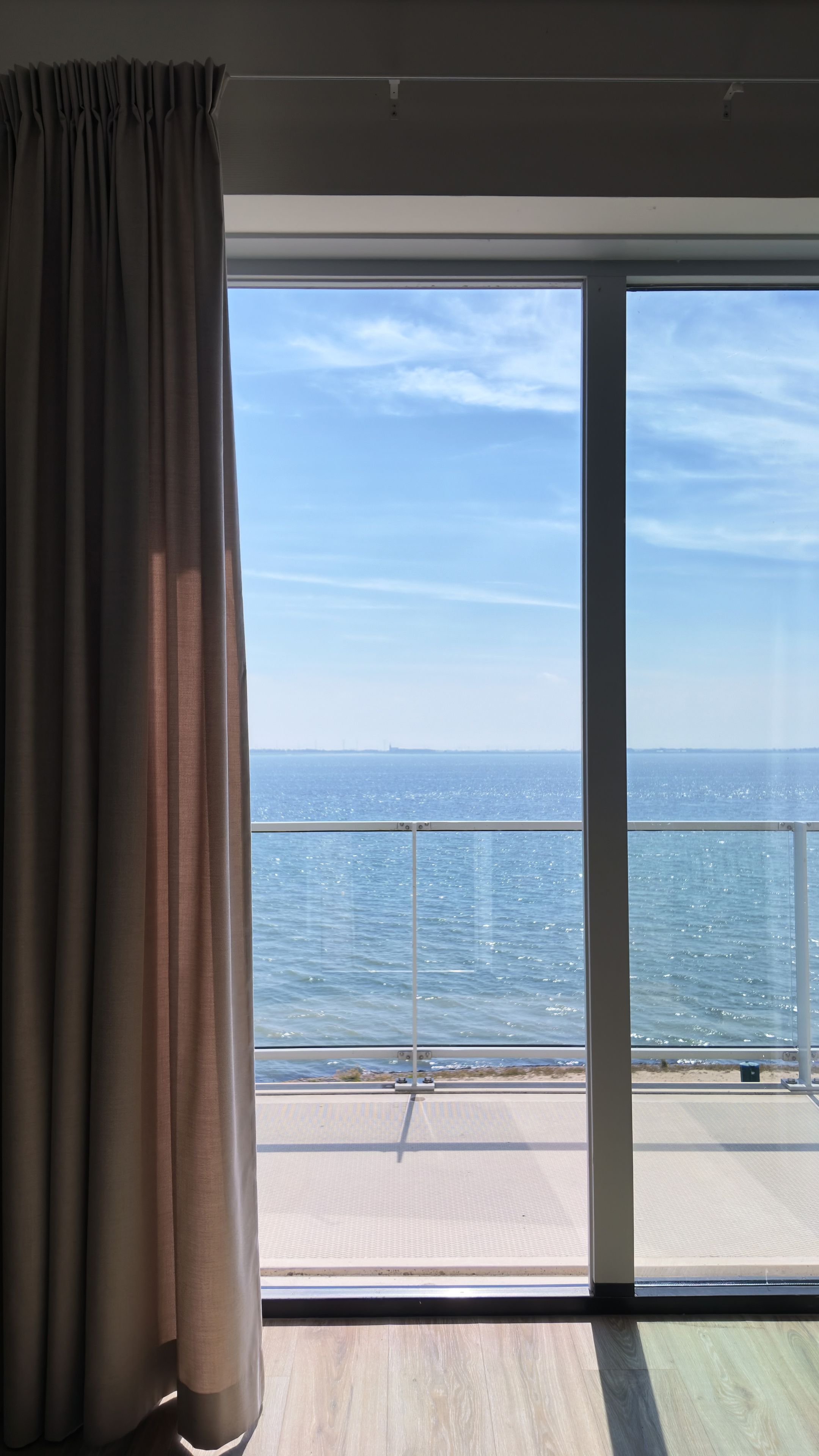 Una stanza con un'ampia porta-finestra scorrevole che dà su un balcone con vista su un corpo d'acqua.