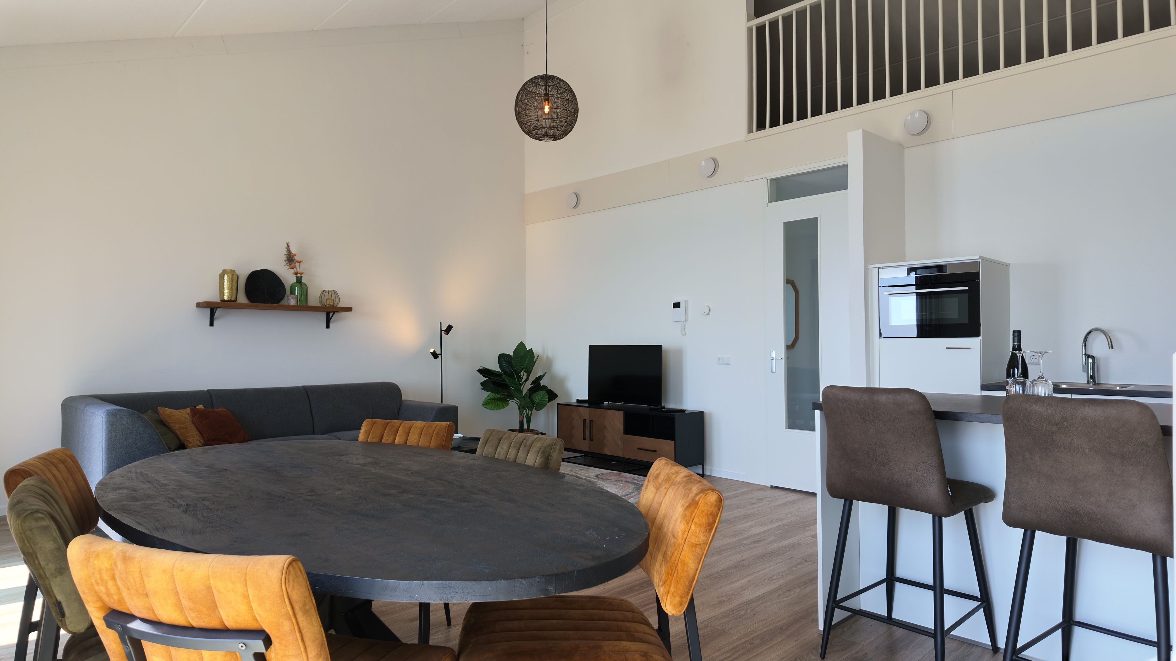 Een moderne woonruimte met een ronde eettafel, banken en een keukenhoek.