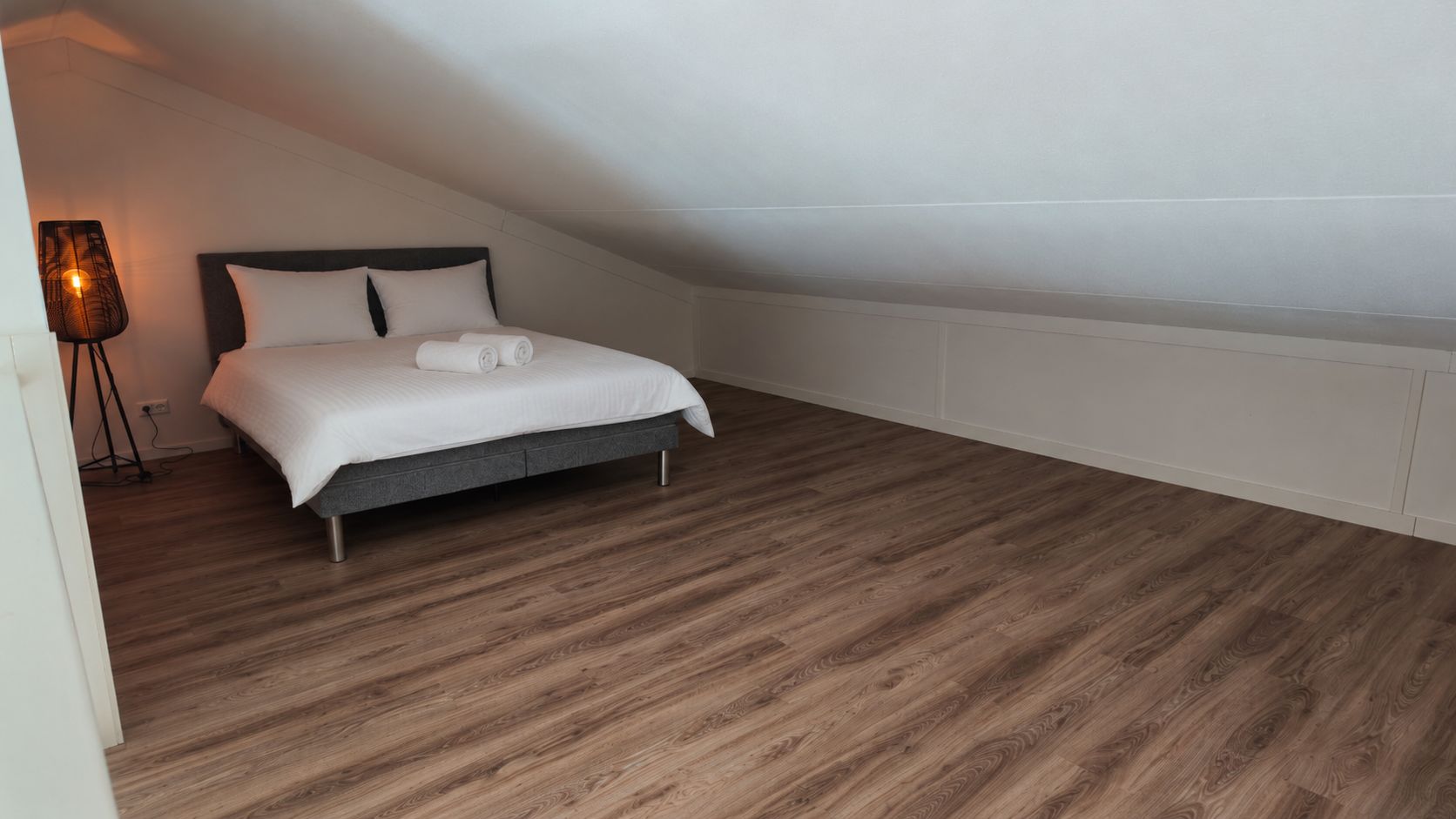 Una camera da letto con un letto, una lampada e un pavimento in legno.