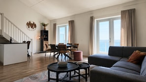Ein modernes Wohnzimmer mit einer Couch, einem Esstisch und Stühlen, einer Küchenzeile mit Arbeitsplatte und Schränken sowie einer Treppe, die in eine obere Ebene führt.