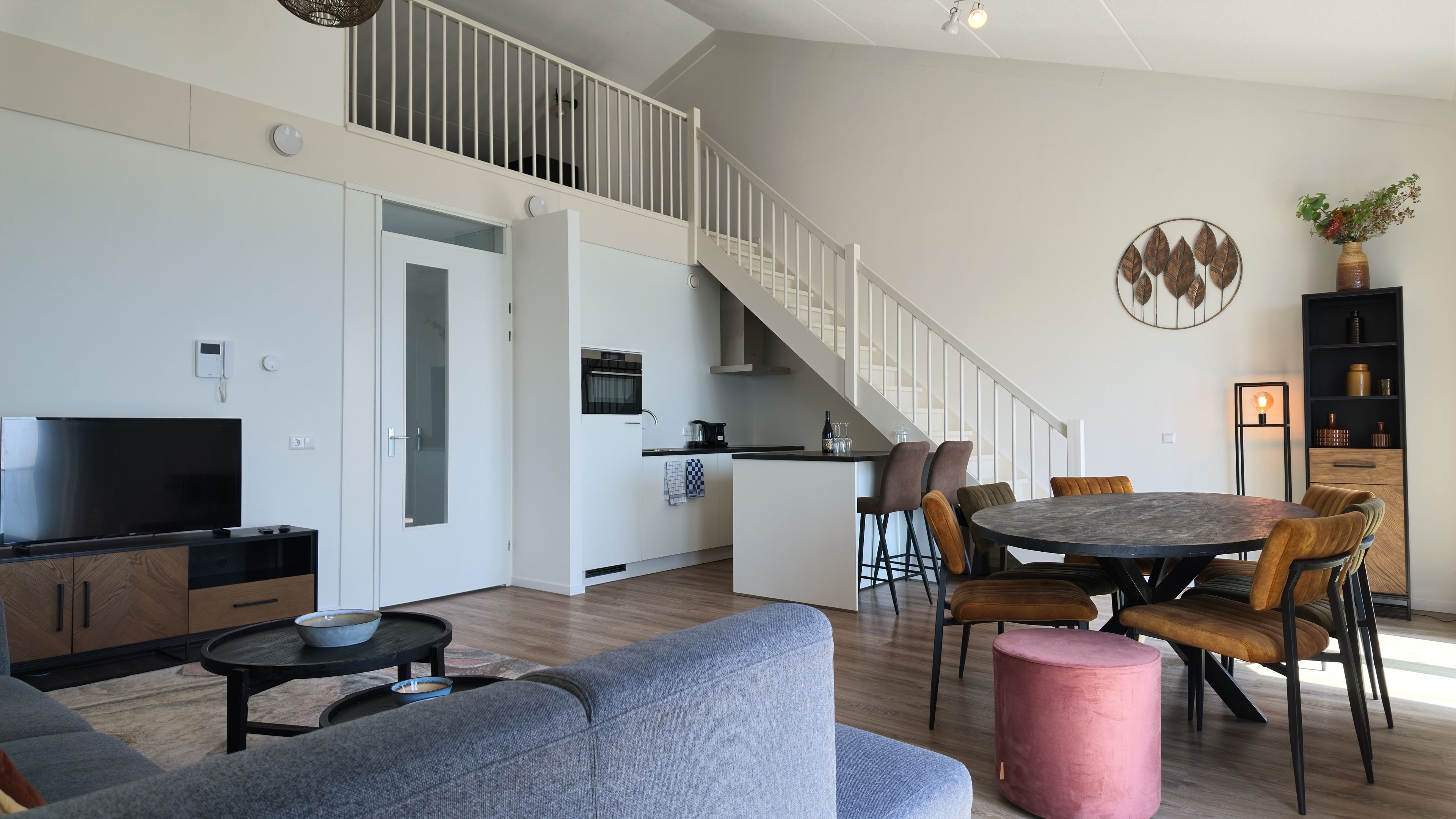 Un espacio habitable moderno con cocina, comedor y una escalera que sube a un nivel superior.