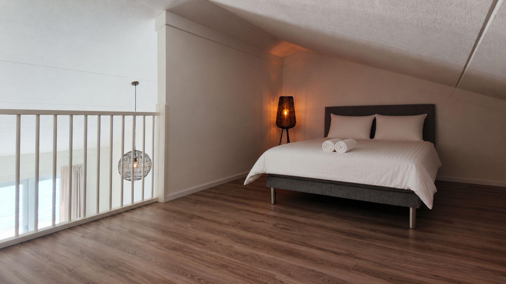 A bedroom with a bed, a nightstand, a lamp, and a view of the outdoors.