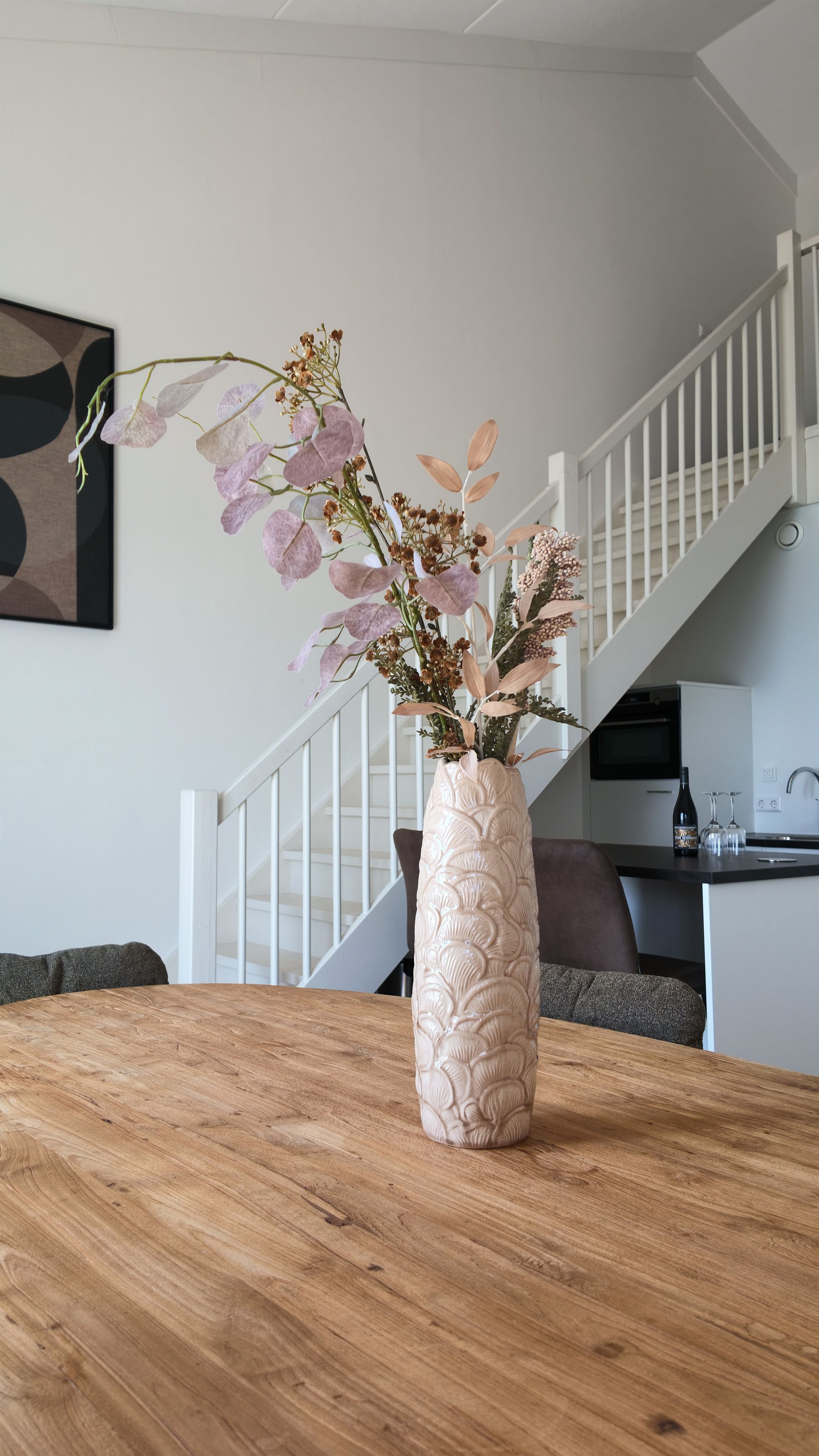 Een houten tafel met een decoratieve vaas gevuld met gedroogde bloemen en planten.