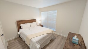 A bedroom with a bed, a nightstand, a window with blinds, and a bedside table with a tissue box.