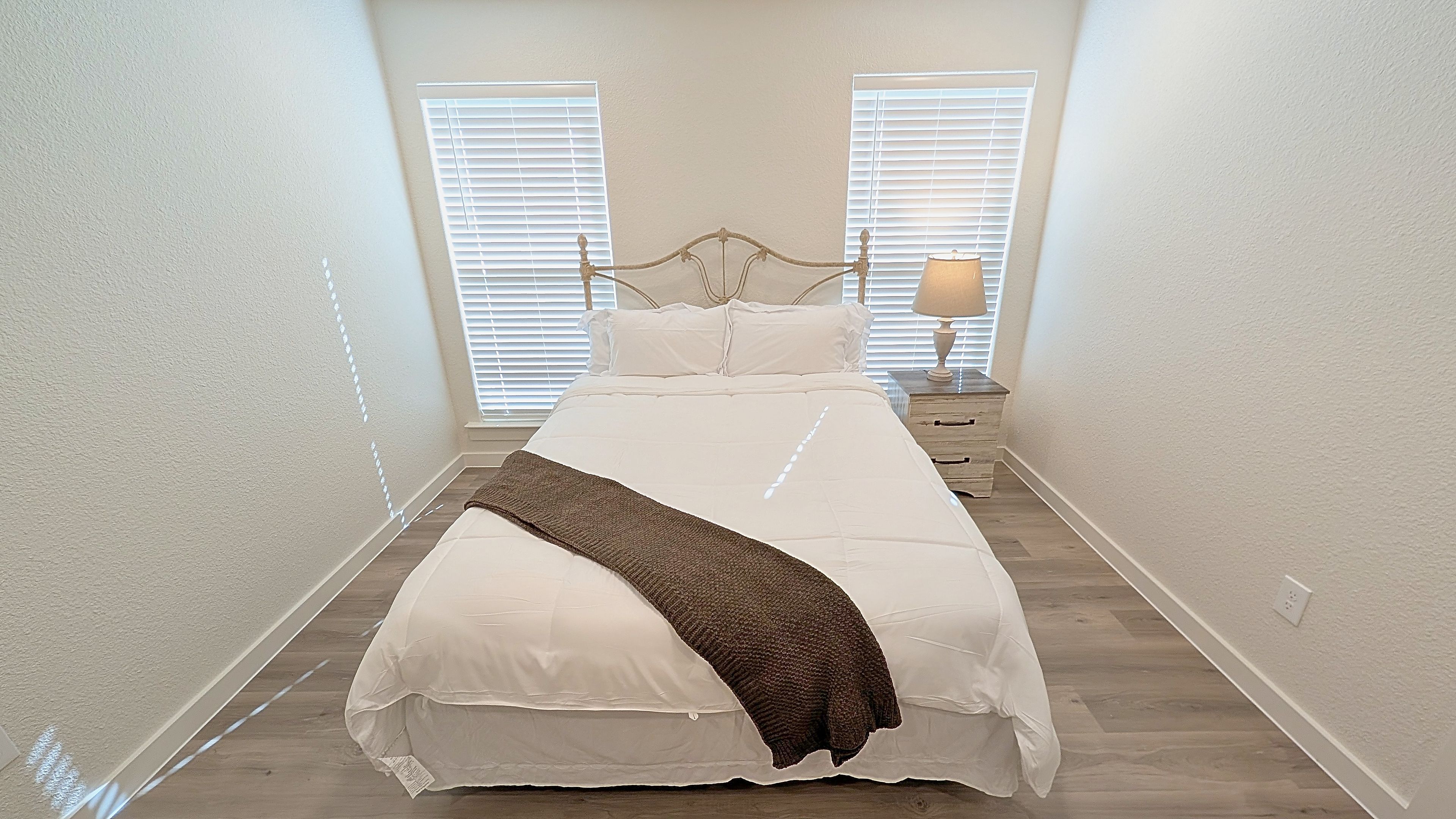 A bedroom with a bed, two bedside tables, a lamp, and a window with blinds.