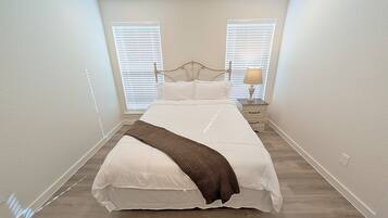A bedroom with a bed, two bedside tables, a lamp, and a window with blinds.
