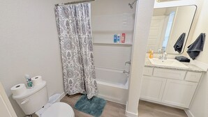 A bathroom with a toilet, shower, sink, and a mirror. - Lubbock Launchpad Retreat (Lubbock)