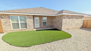 A residential building with a brick facade, a sloped roof, and a small front yard with artificial grass and gravel. - Lubbock Launchpad Retreat (Lubbock)