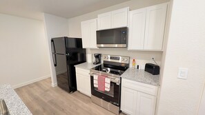 A compact kitchen with a black refrigerator, microwave, stove, and oven.