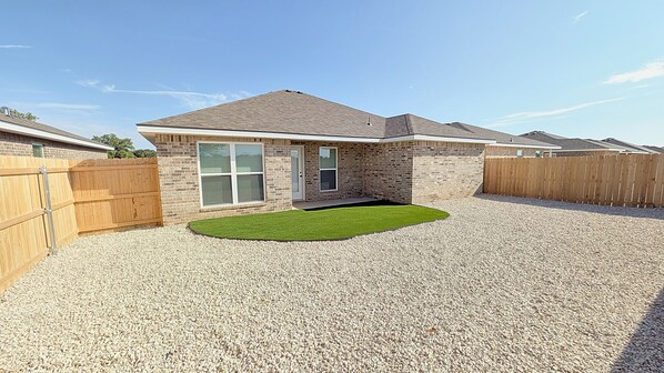 A residential house with a brick exterior, a gravel driveway, and a small lawn area.