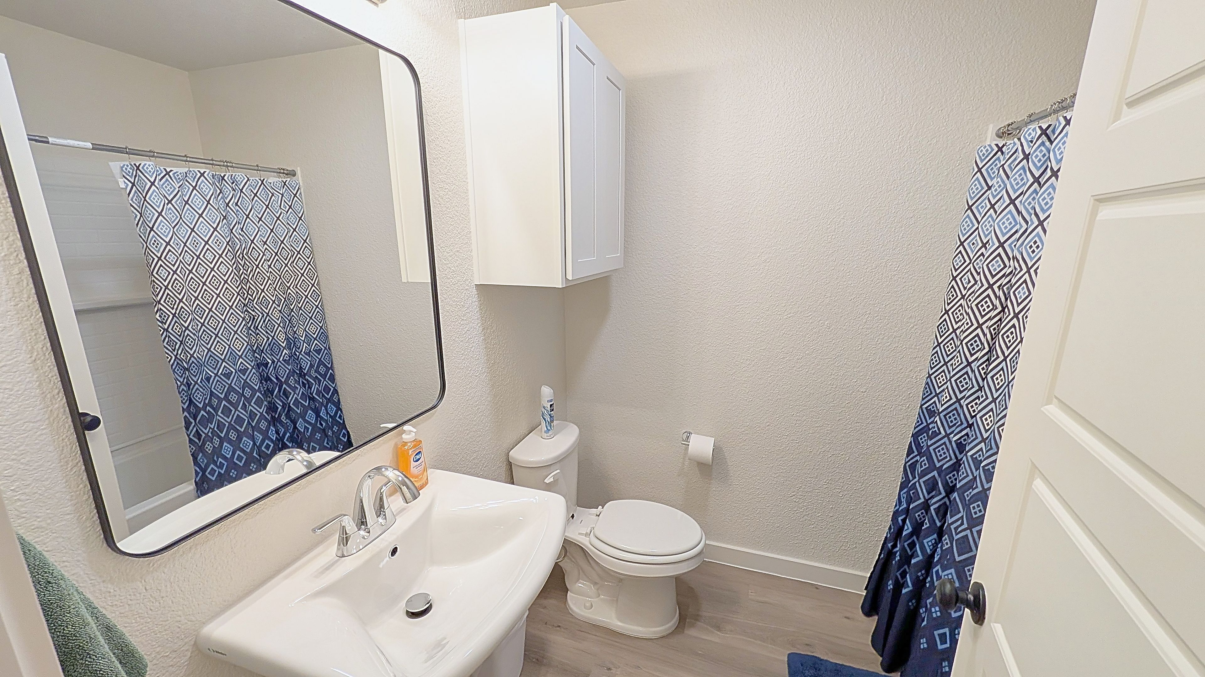 A bathroom with a sink, toilet, mirror, and patterned shower curtain.