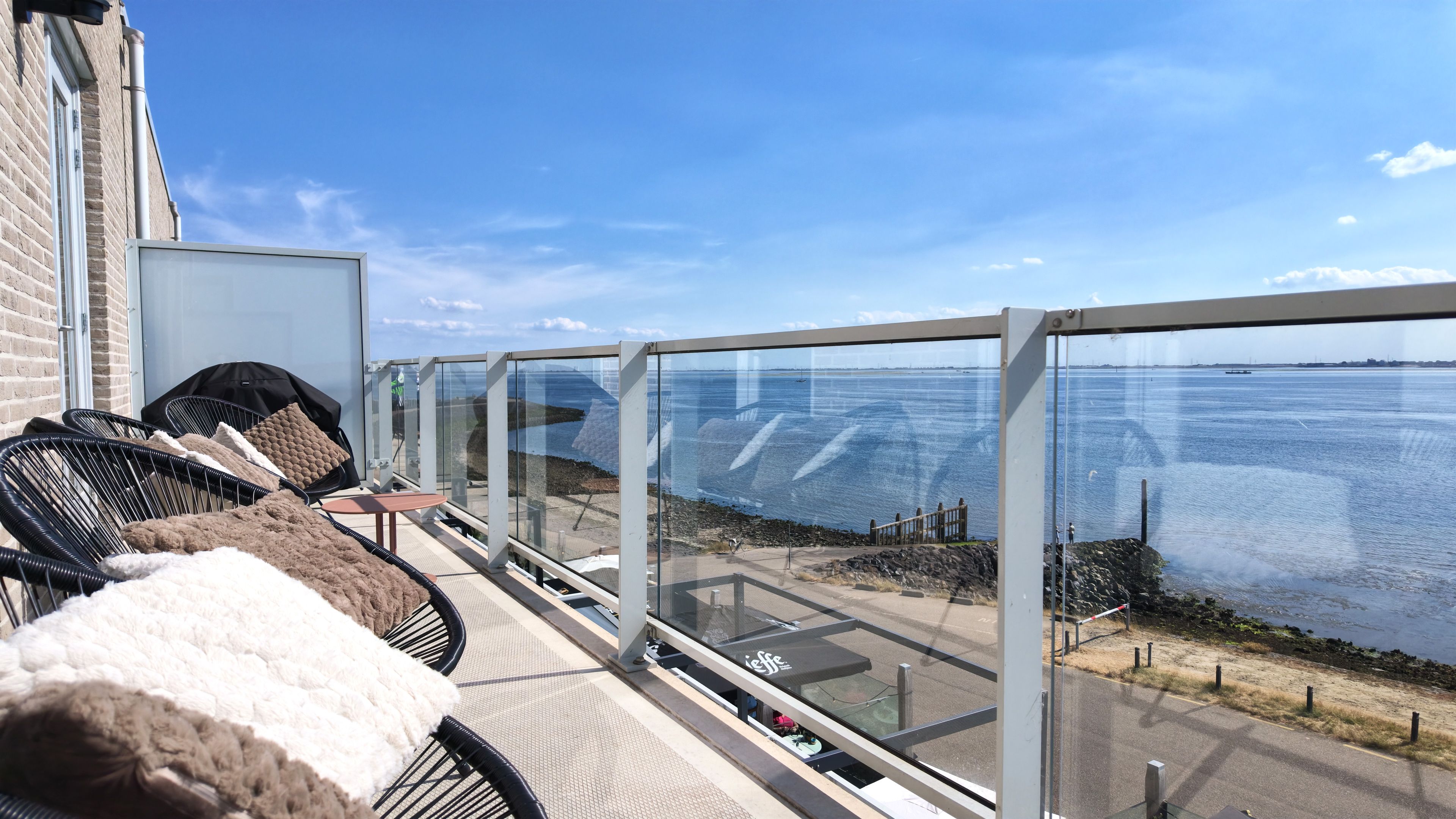 Un balcone con posti a sedere all'aperto, vista sul mare e un edificio con facciata in mattoni.