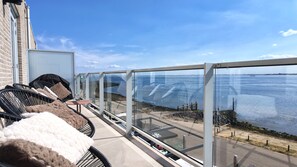 Un balcón con mobiliario exterior, vista al mar y un edificio con fachada de ladrillo.