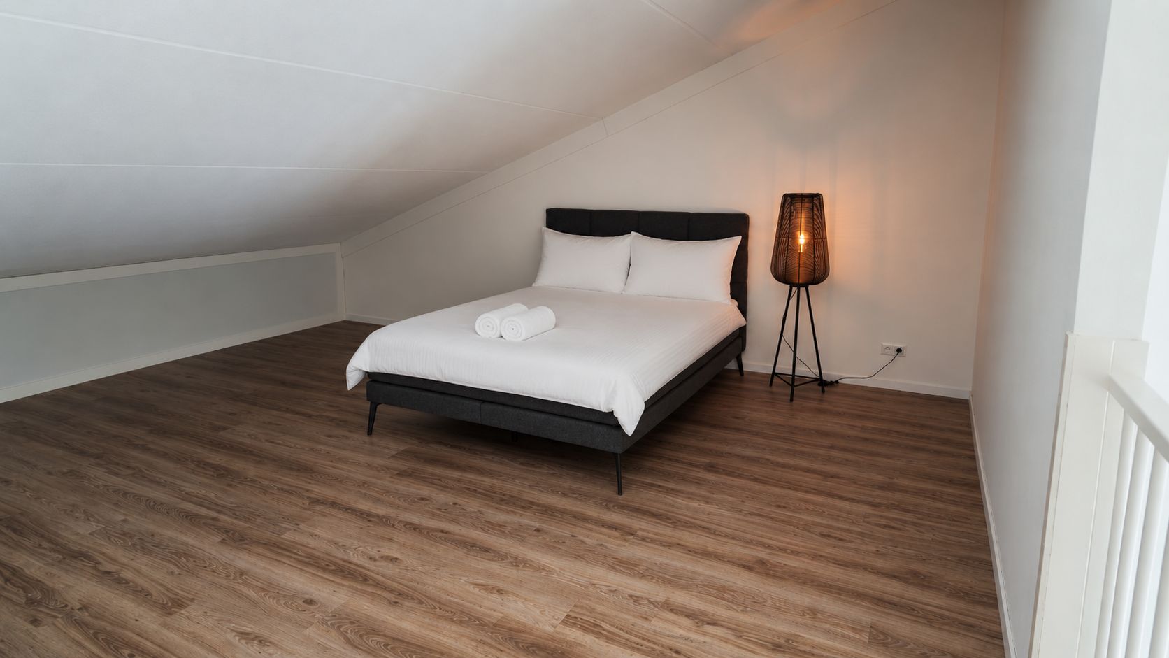 Een slaapkamer met een bed, een bedlampje en een houten vloer.