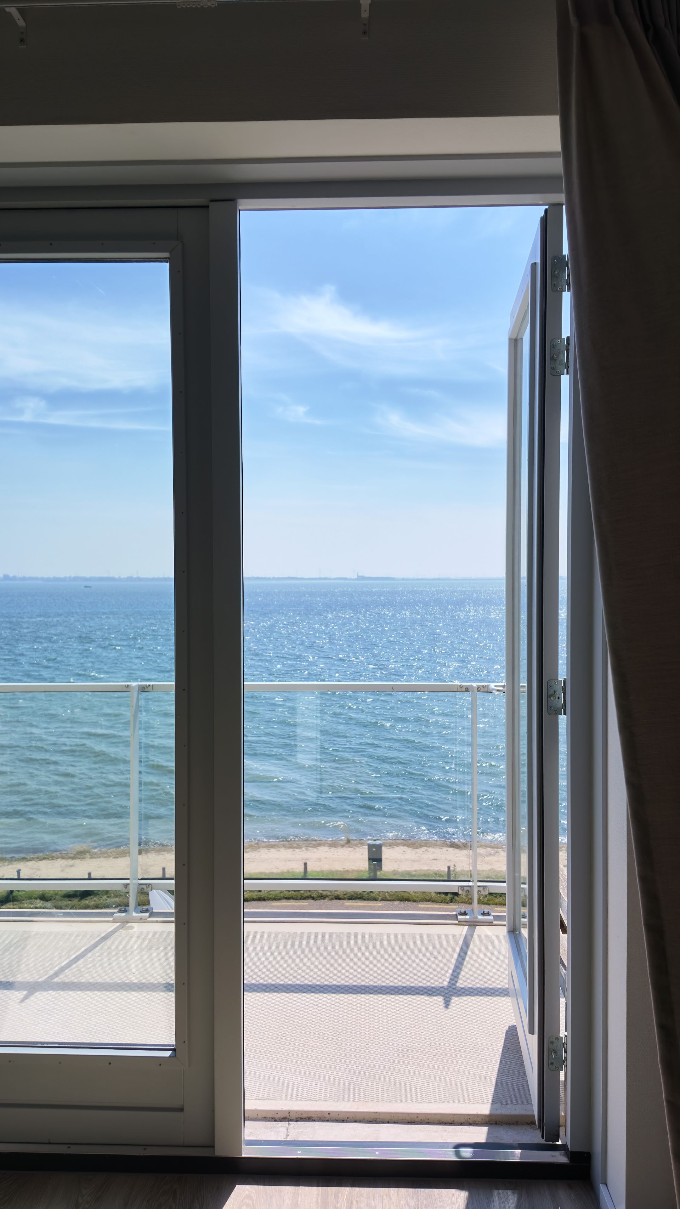 Una stanza con un'ampia porta-finestra scorrevole che si apre su un balcone con vista sulla spiaggia e sul mare.