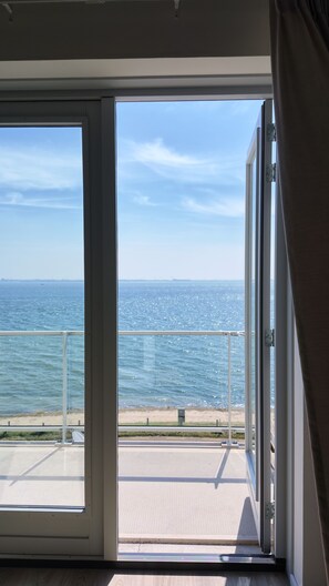 Una habitación con un amplio ventanal corredero que da a un balcón con vistas a la playa y al mar.